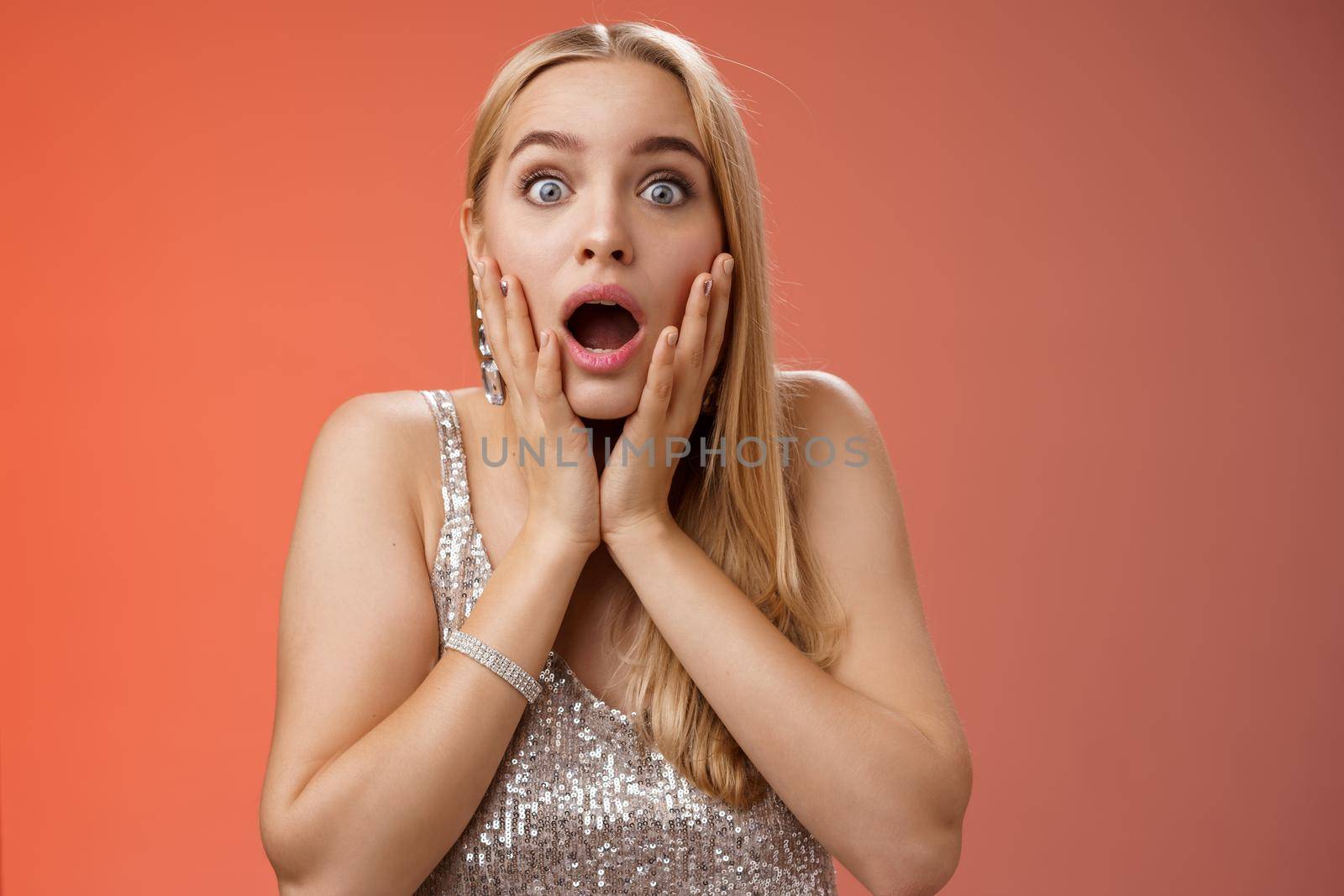 Shocked speechless concerned young stunned woman gasping screaming worried drop jaw touch cheeks widen eyes surprised nervously staring camera troubled afraid, standing red background.