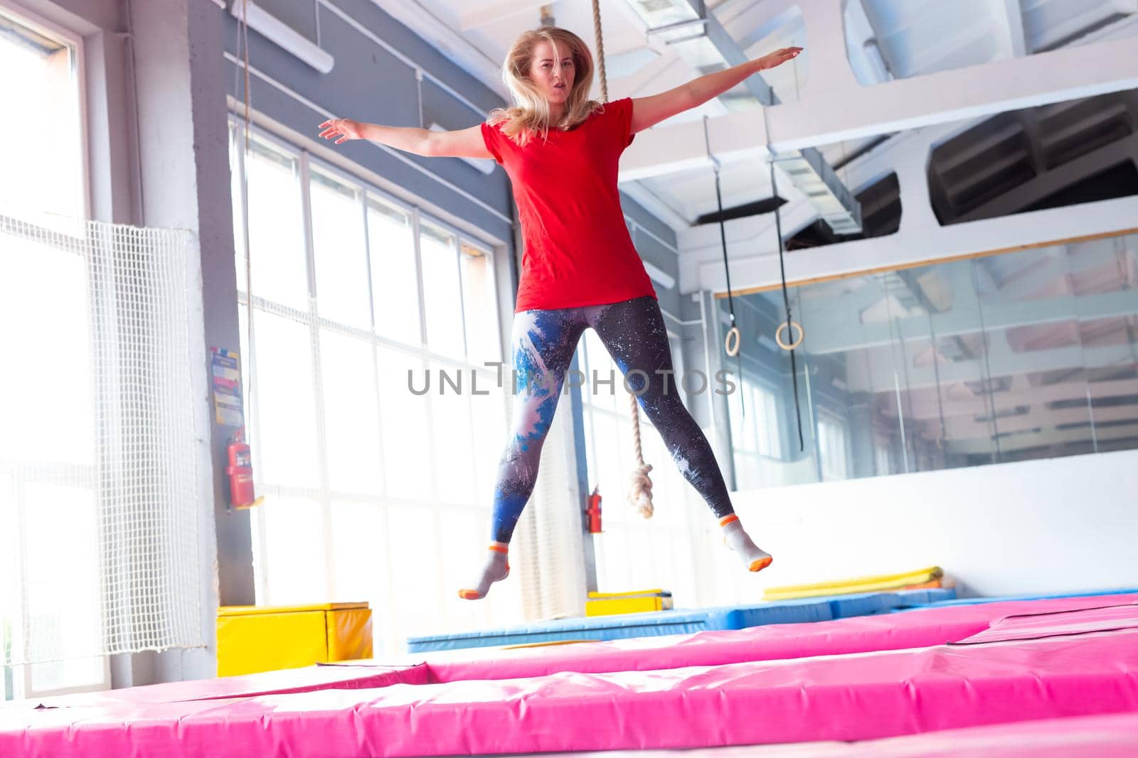 Fitness, fun, leisure and sport activity concept - Young happy woman jumping on a trampoline indoors.