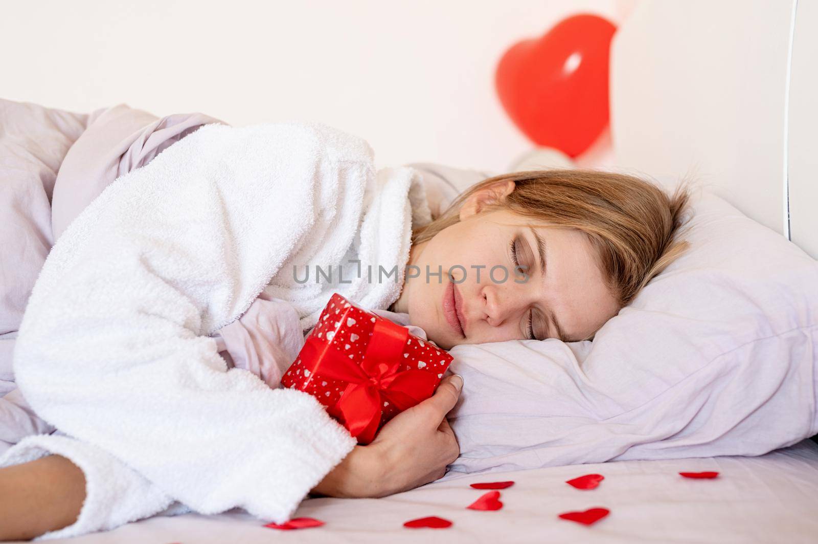 young blond woman lying in bed with holiday gift and red balloons by Desperada