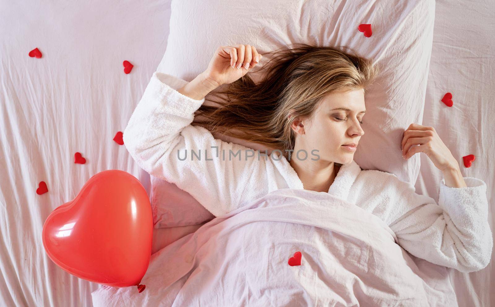 Happy valentines day. young blond woman sleeping in bed with holiday gift and red confetti