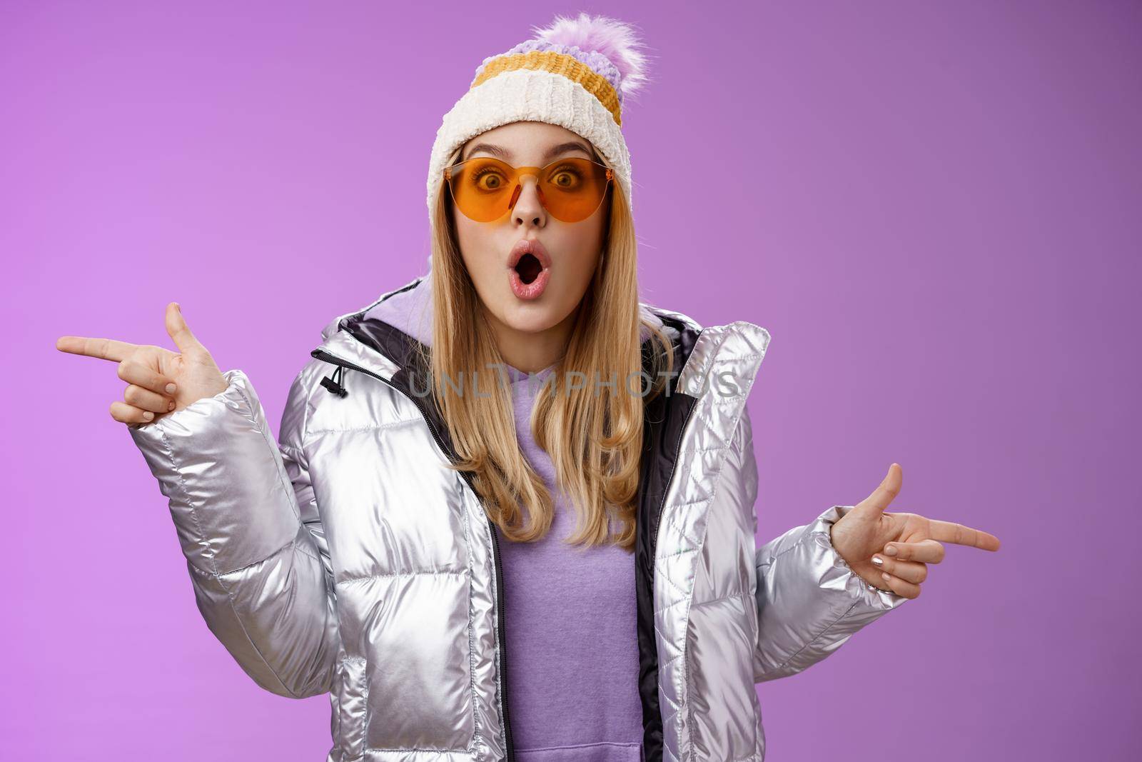 Impressed blond girl gasping widen eyes surprised folding lips wow sound check out incredible discounts winter equipment pointing left right cannot choose standing astonished purple background.
