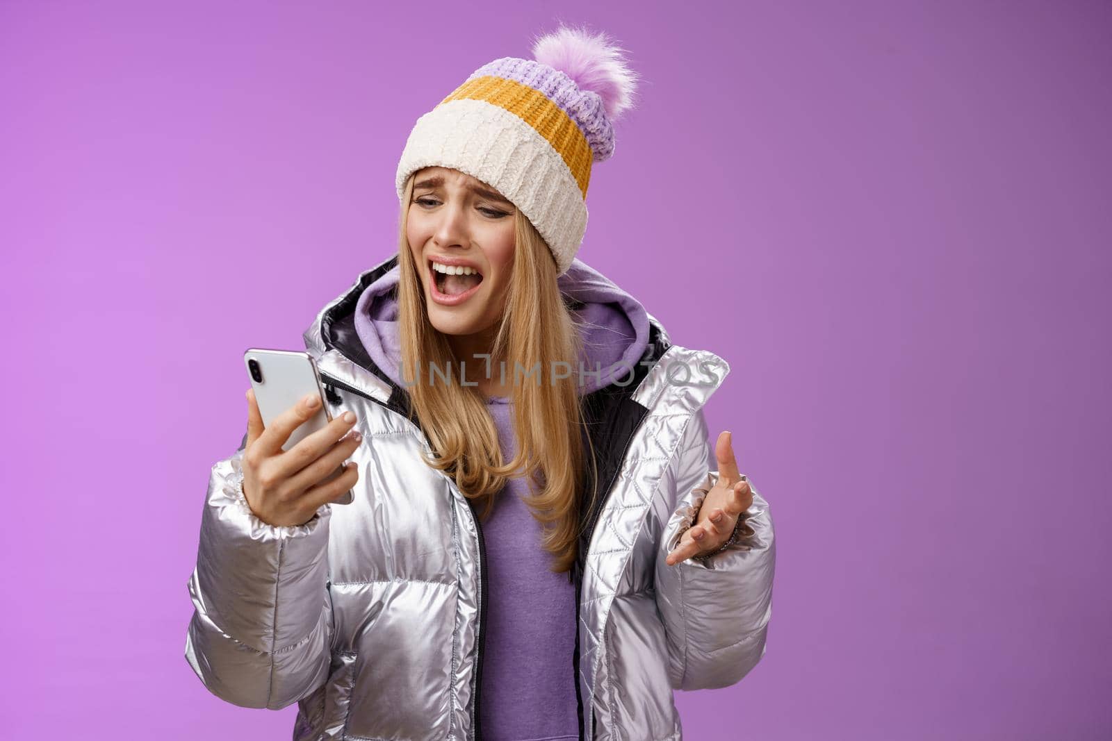 Bothered complaining dissatisfied cute blond girl yelling stupid smartphone standing unhappy recording audio message whining yelling mobile phone upset, standing purple background. Technology concept