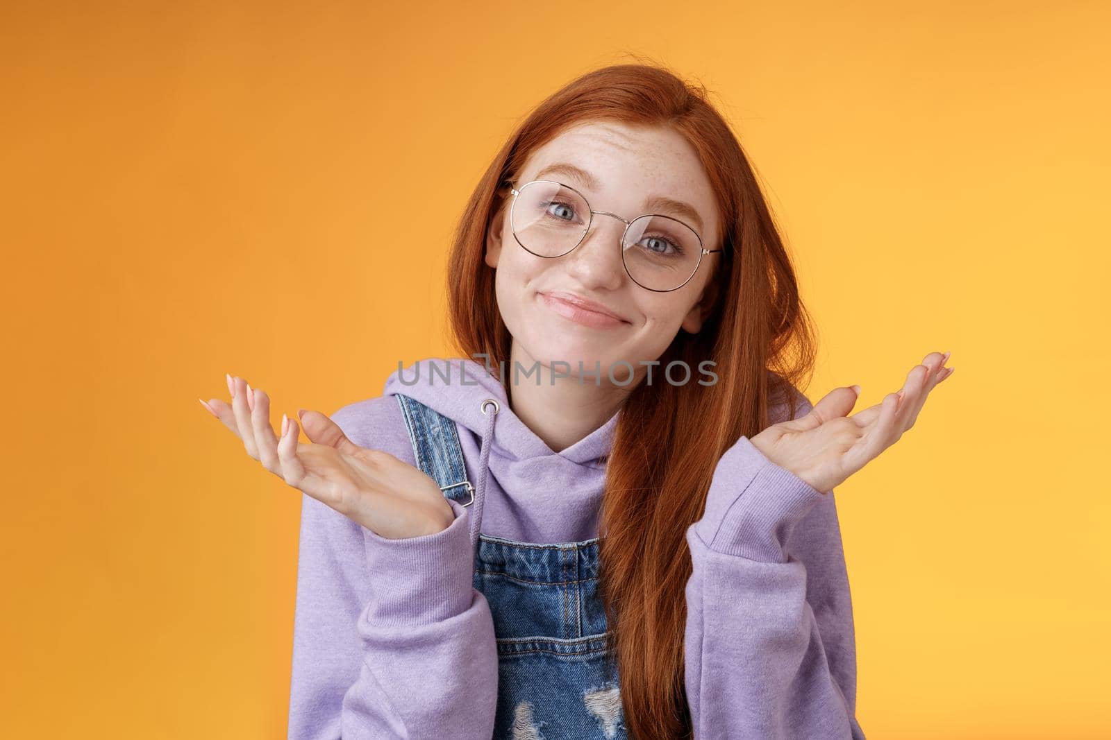 Nothing much. Attractive silly unsure carefree redhead unbothered cute female wearing geek glasses smirking uncertain shrugging hands spread sidways clueless what do future, orange background by Benzoix