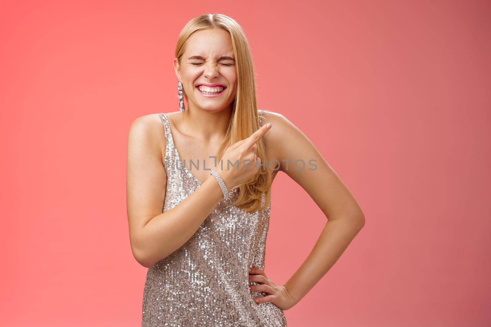 Carefree joyful blond attractive woman having fun joking laugh hilarious boyfriend outfit close eyes giggling smiling broadly pointing upper right corner behind standing red background by Benzoix