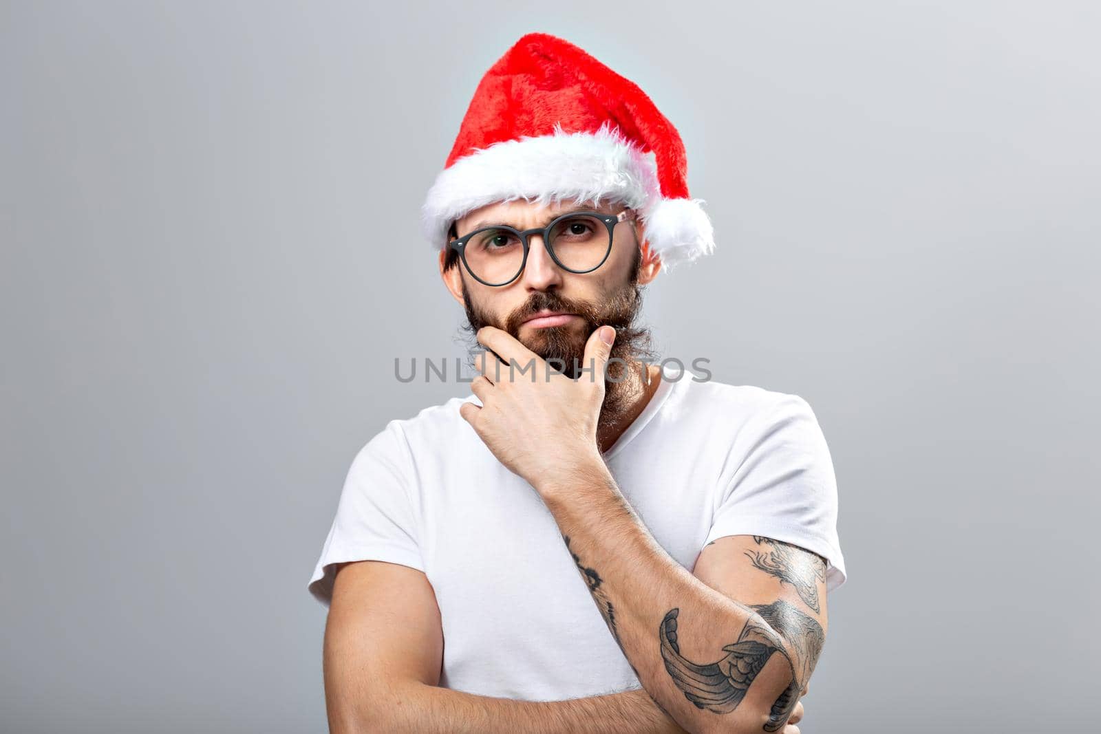 Holidays and people concept - Portrait of a handsome brutal man in Christmas hat. Over grey background