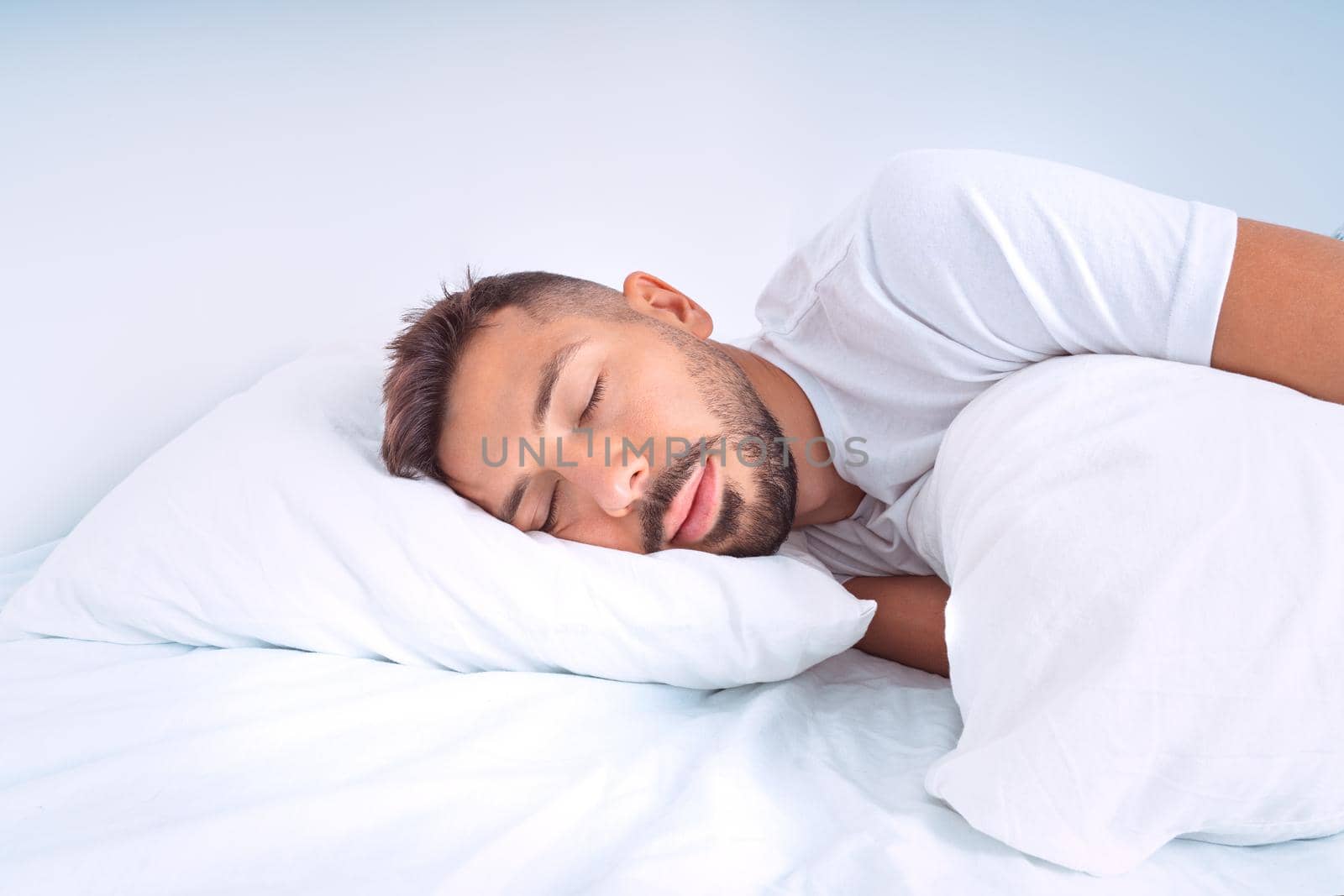 Handsome cute man sleeping in the bed with white beddings. Man lying on the pillow and enjoying good healthy sleep. High quality photo
