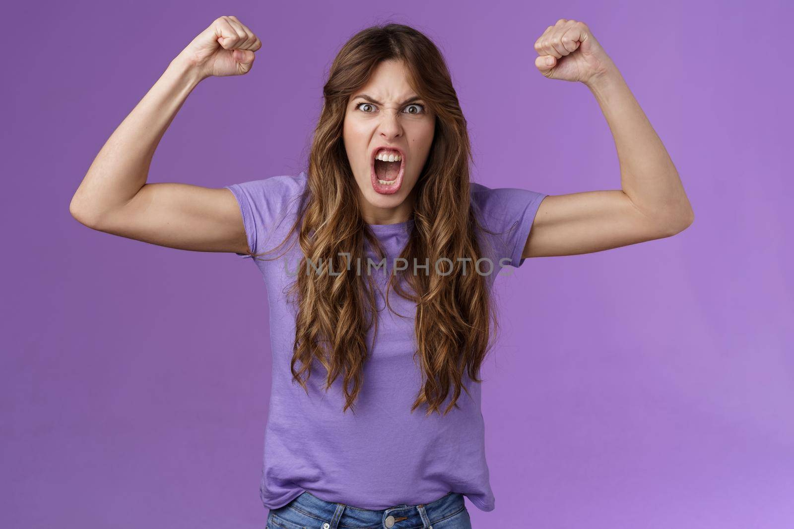 Funny curly-haired girl raising hands fist pump show muscles yelling daring cool shouting encouraged motivated win grimacing strong powerful woman celebrating victory feel like champion. Lifestyle.