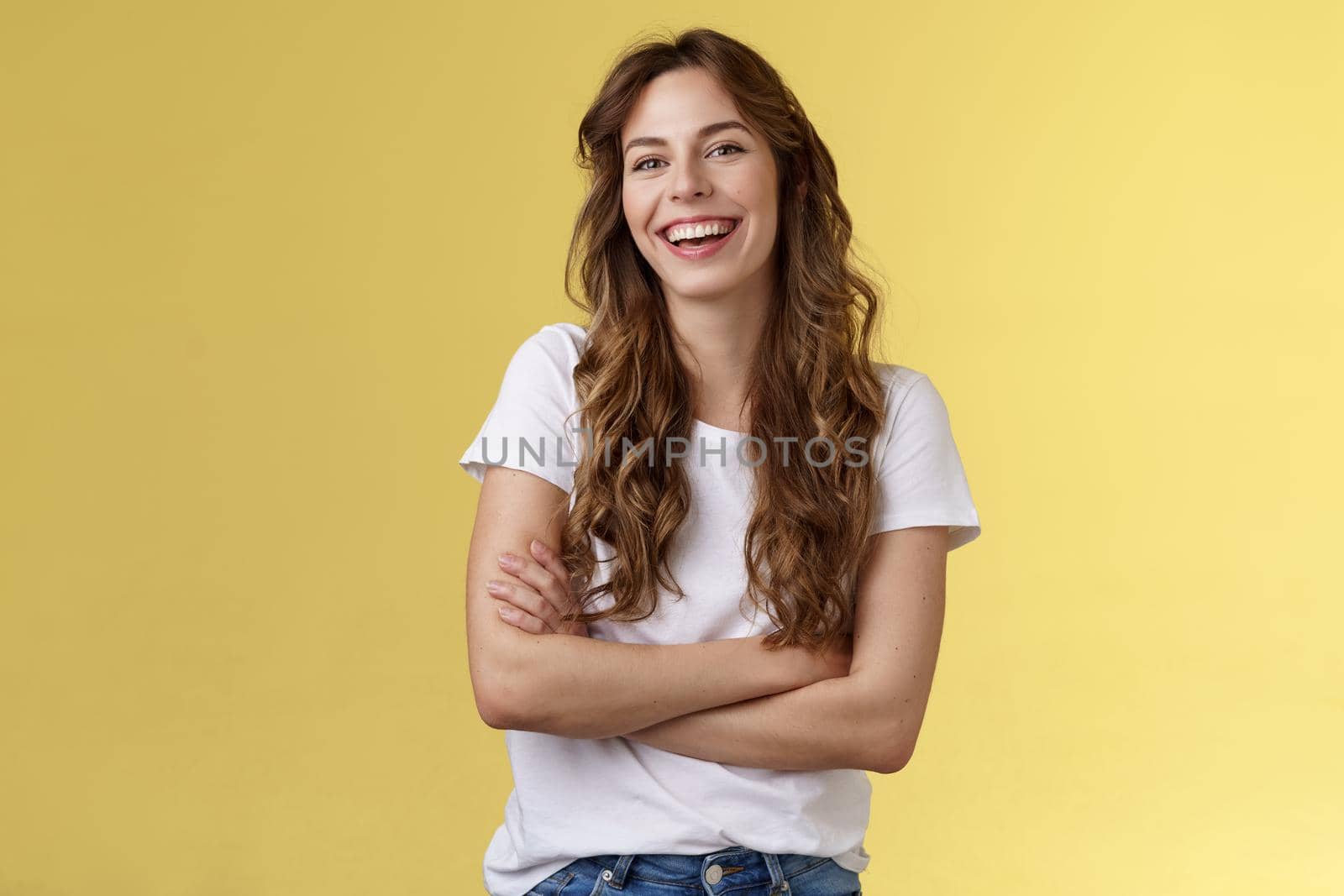 Entertain me. Friendly charismatic female long curly haircut laughing joyfully hang out friends cross arms chest feel chilly slightly cold have amusing pleasant conversation yellow background.