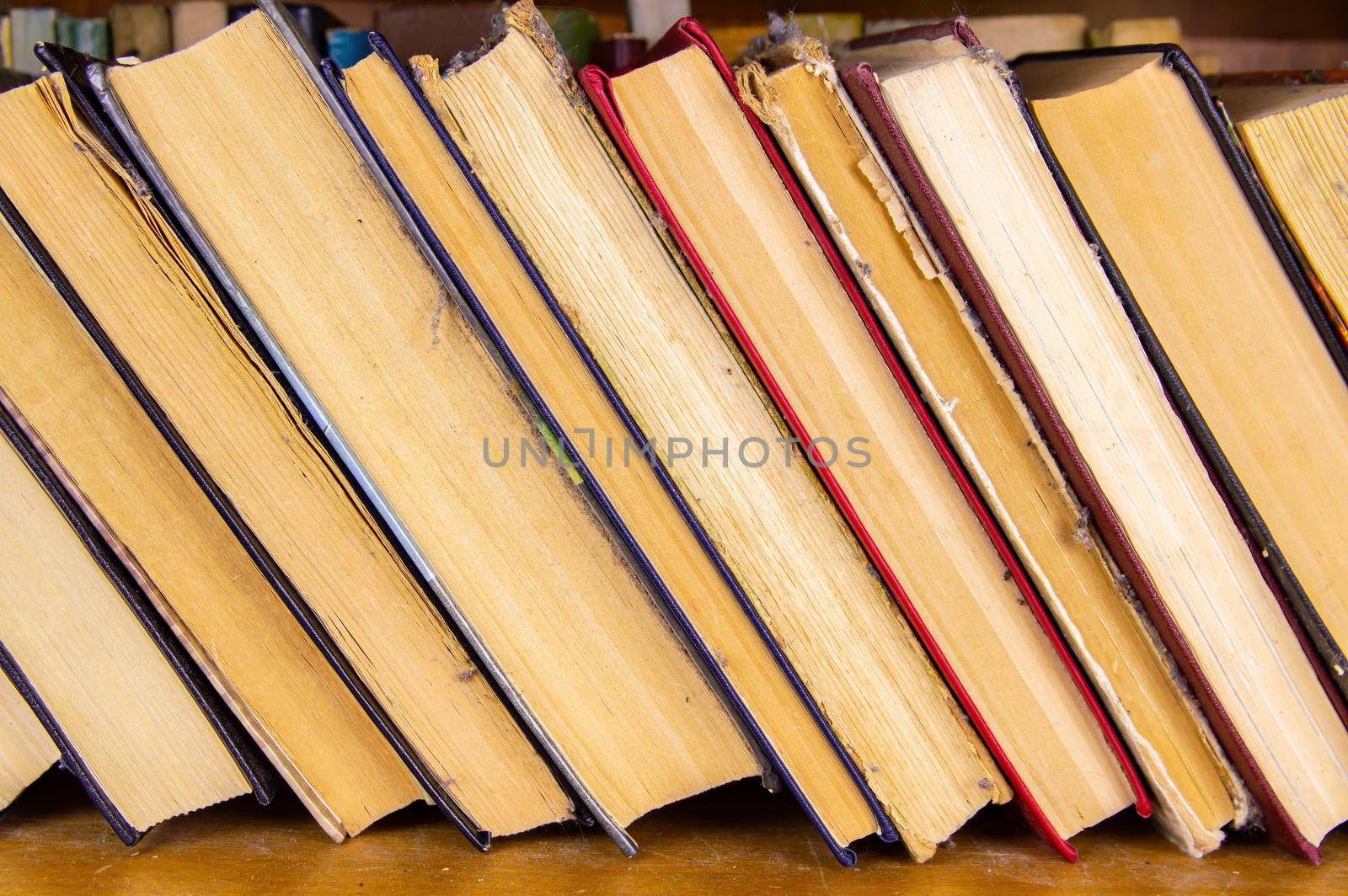 Old stack of books on the bookshelf. Old books in a row. Book binding. Bookshelf. Yellow paper pages. Literary edition. Background image. Free space for text.