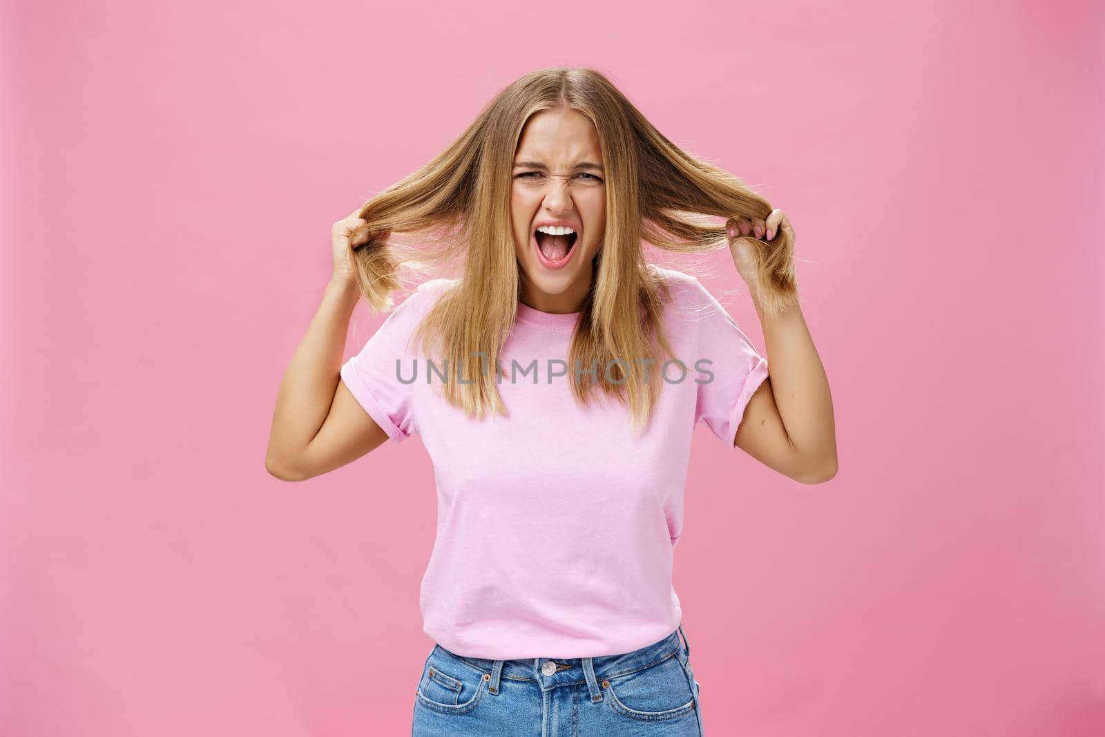Portrait of pissed outraged and irritated woman losing temper feeling pressured screaming from distress pulling hair out of head standing annoyed over pink background fed up doing haircut every day by Benzoix