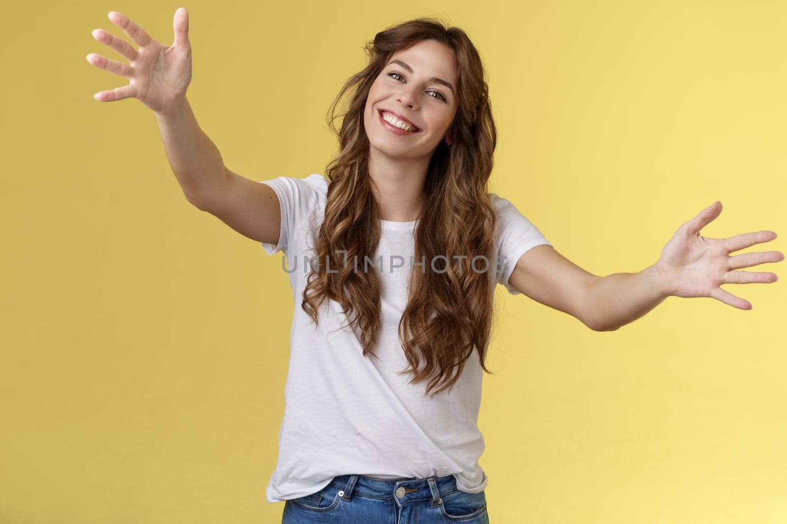 Wanna hold you tight. Romantic sincere gentle cute caucasian girl long beautiful curly hair tilt head lovely extend arms give cuddles wanna hug friend embracing dear guests yellow background.