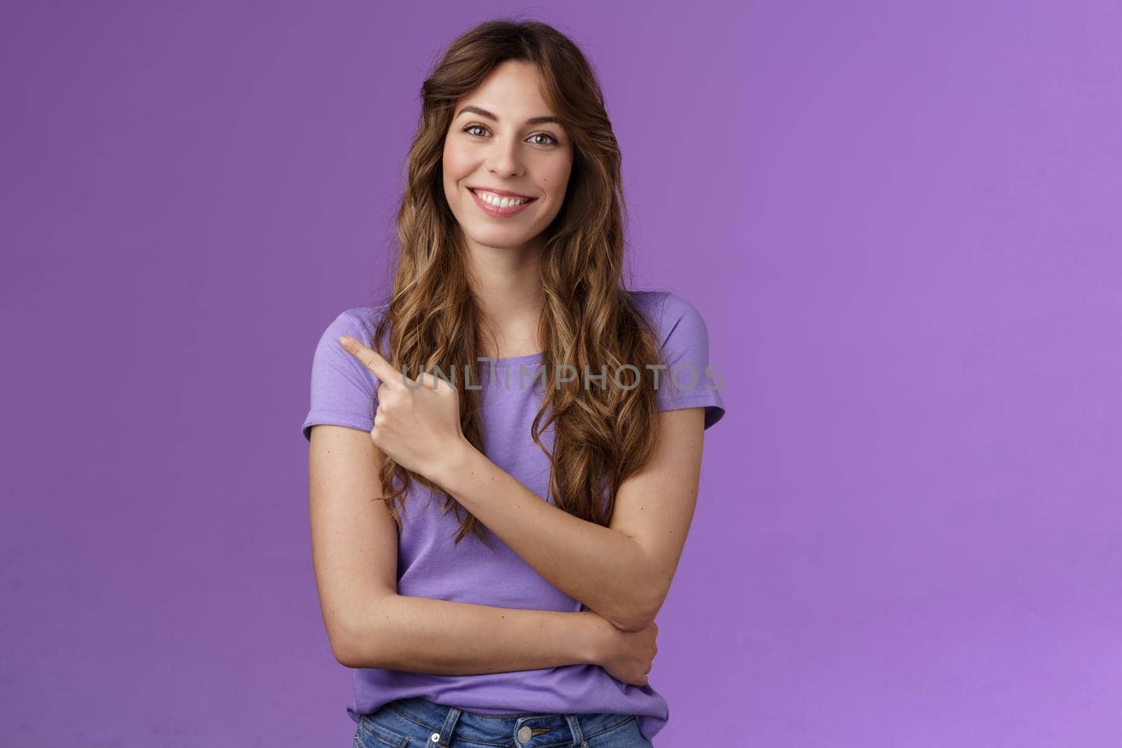Cheerful smart confident assertive curly-haired caucasian female share link pointing index fingers upper left corner smiling broadly give advice what place visit stand purple background by Benzoix