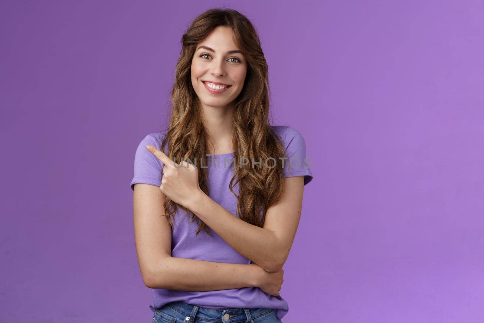 Cheerful smart confident assertive curly-haired caucasian female share link pointing index fingers upper left corner smiling broadly give advice what place visit stand purple background. Lifestyle.