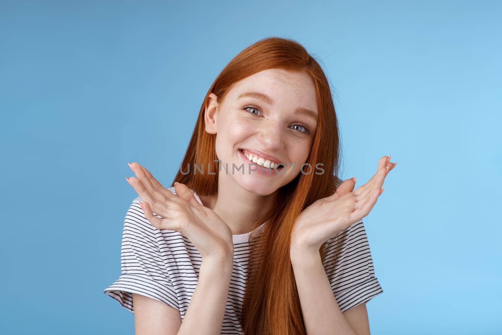Silly cute sincere young european ginger girl blue eyes shrugging hold hands doubtful spread near face tilting head apologizing flirty say sorry late making lame excuses, standing blue background.