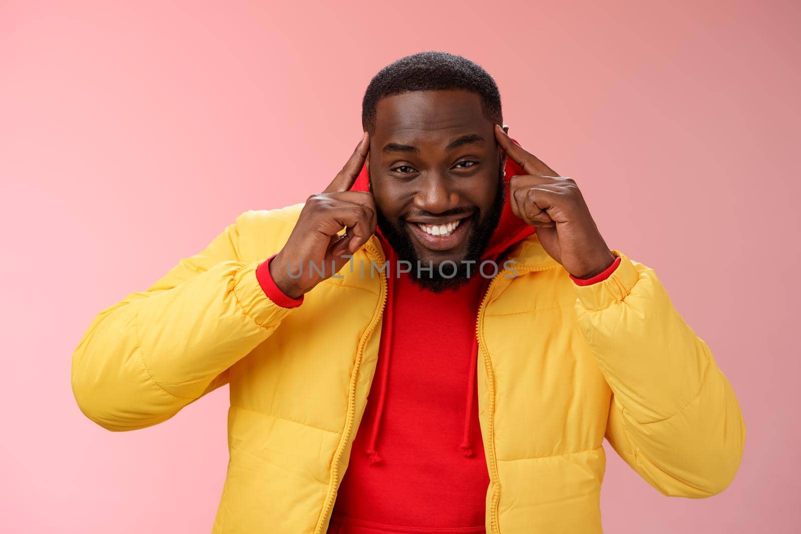 Think about it. Portrait charming creative young happy african guy bearded hold index fingers temples brain smiling broadly share awesome idea great thought, grinning silly standing pink background.