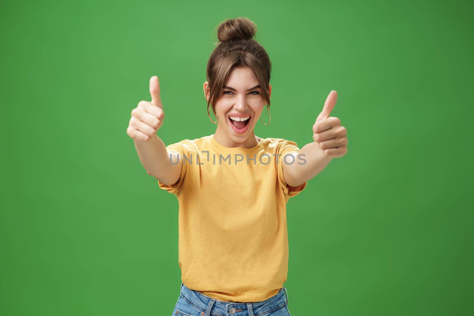 Portrait of cheerful enthusiastic and excited emotive beautiful european woman in yellow t-shirt pulling hands with thumbs up towards camera smiling broadly, being supportive, liking idea. Body language concept