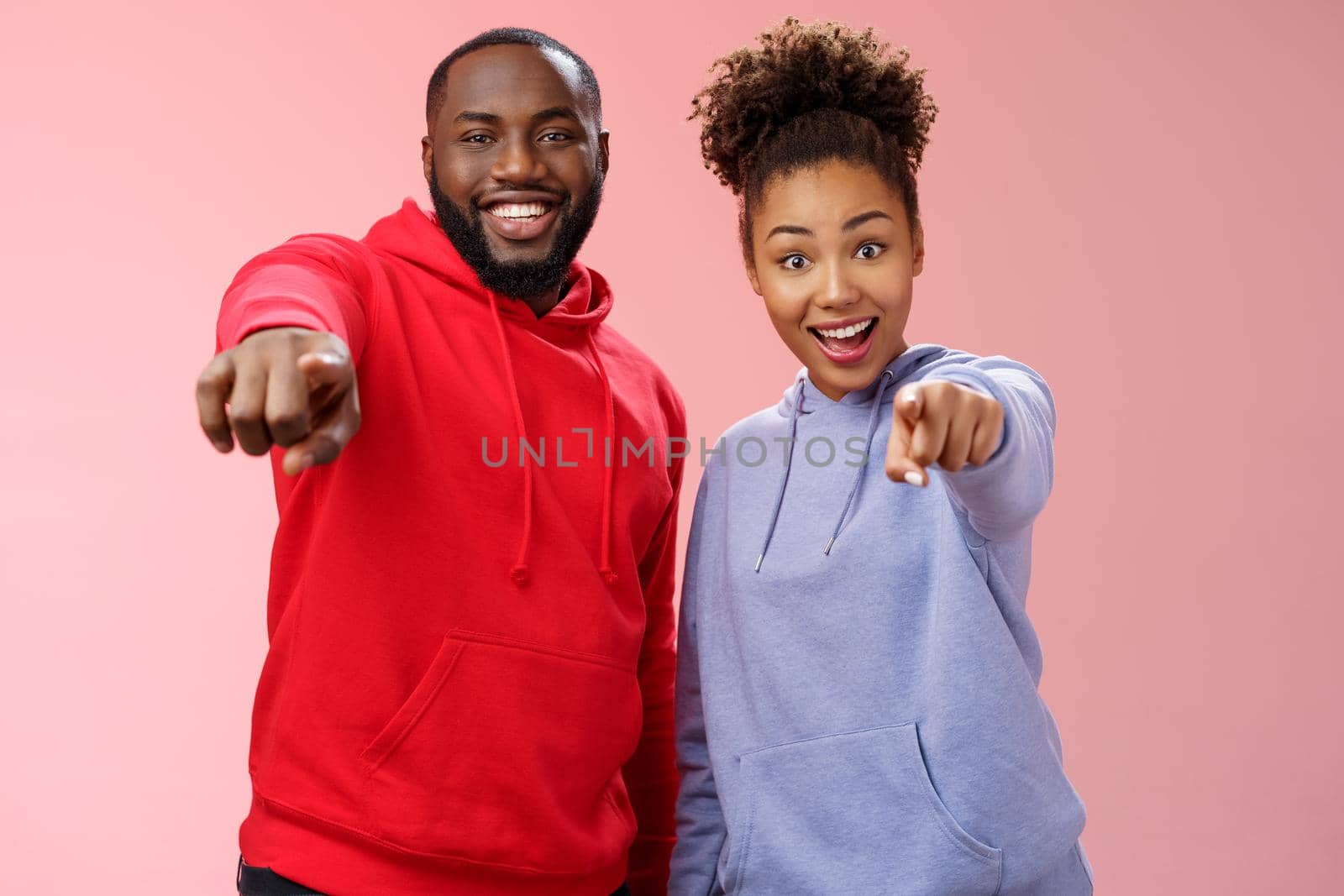 Joyful young attractive happy african-american couple vacation enjoying interesting tour standing impressed amazed pink background pointing index fingers camera awesome curious object.