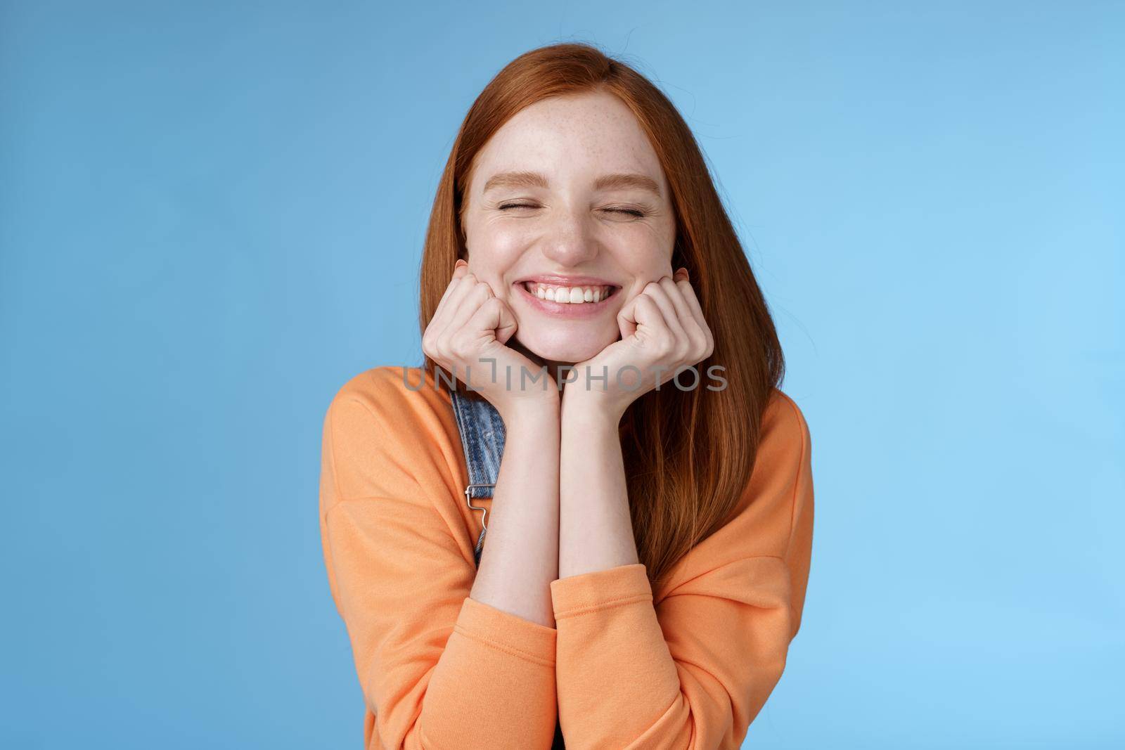 Lifestyle. Silly cute happy redhead girlfriend smiling broadly close eyes dreamy squeez cheeks delighted asked date guy likes standing blue background rejoicing have fantastic lucky day triumphing.