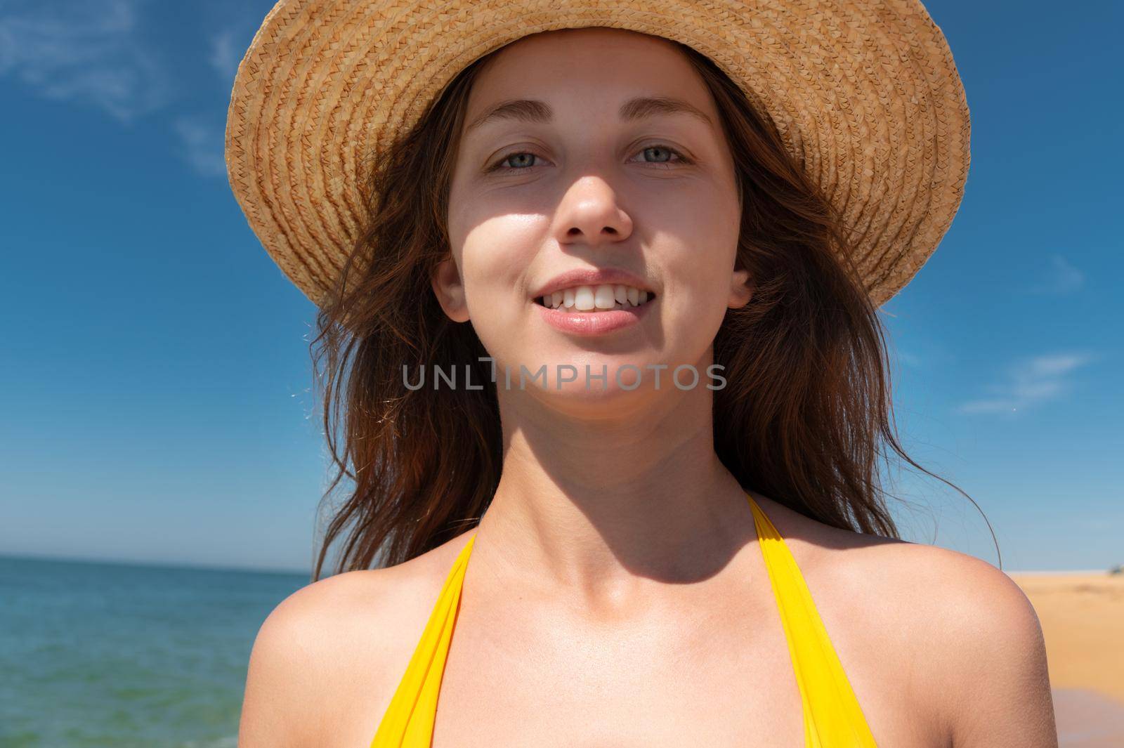 Close-up portrait of attractive caucasian young woman in straw hat and yellow swimsuit smiling against blue sky and sea on a sunny day by yanik88