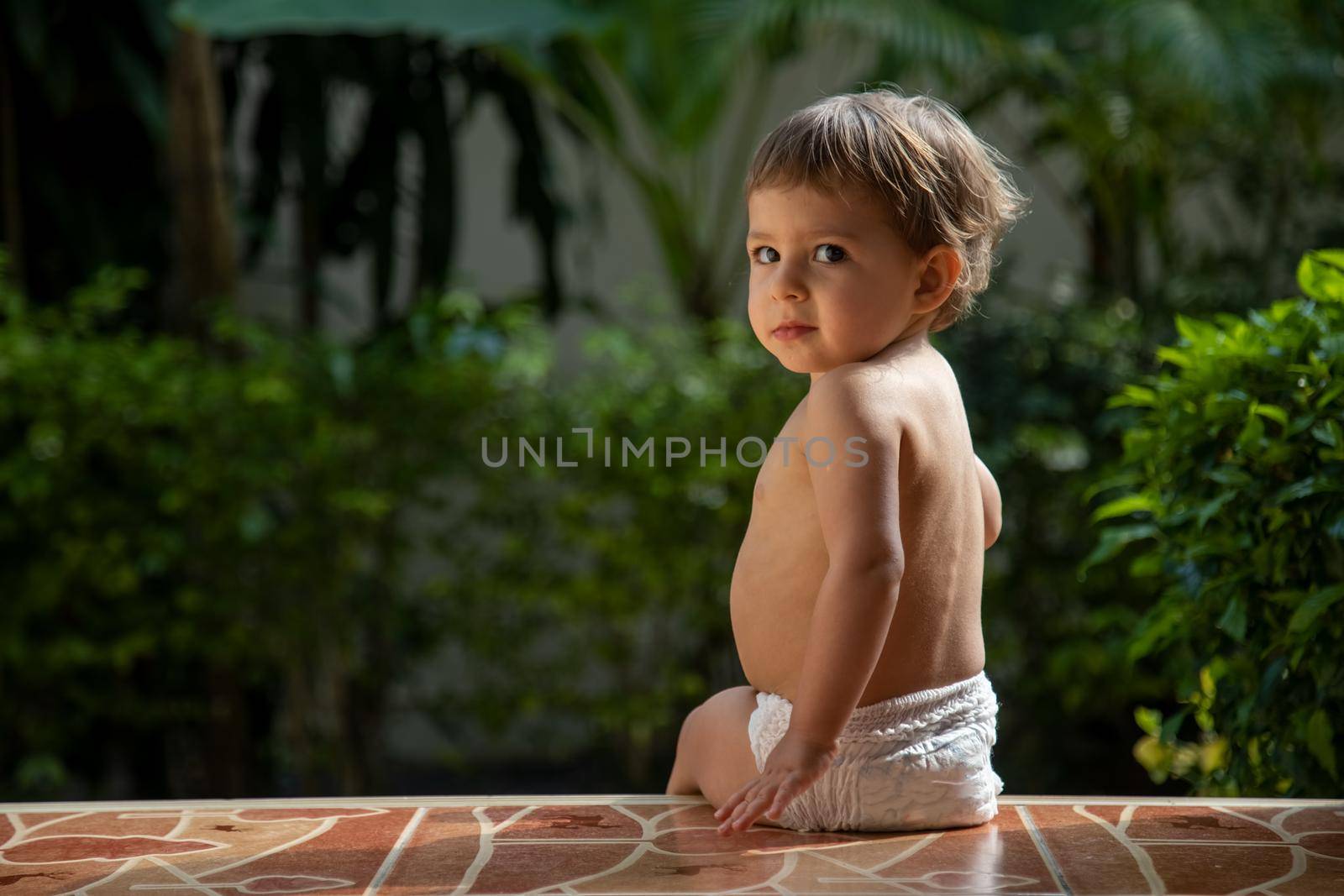 adorable little baby sitting on terrase outdoors summer sunny day rear view