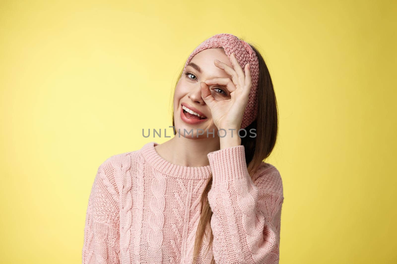 Let me see closer. Cute glamour young stylish european woman wearing knitted sweater, headband tilting head joyfully smiling intrigued positive showing circle over eye peeking at camera playful.