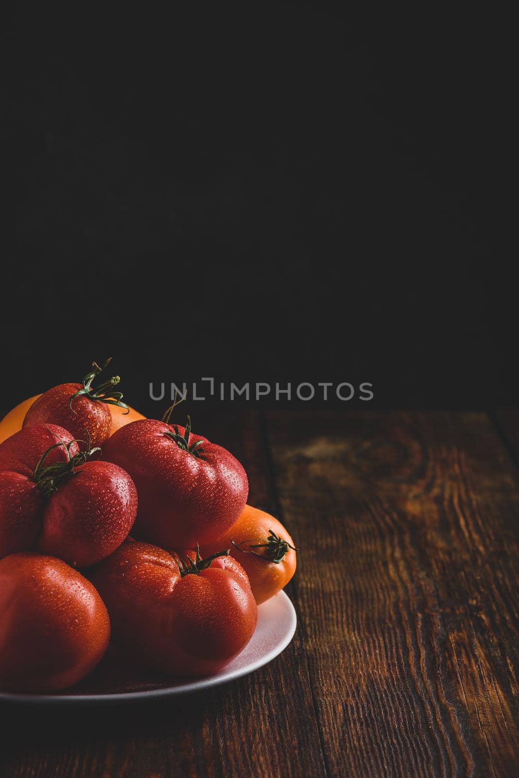 Fresh red and yellow tomatoes on white plate over wooden surface