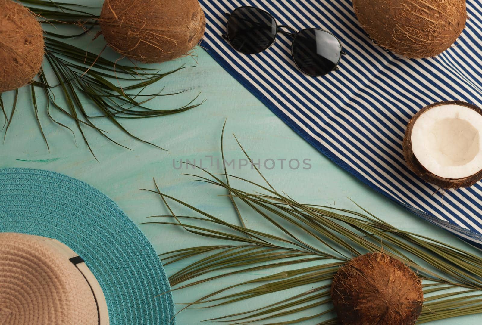 Summer composition or layout. Tropical palm leaves, hat, glasses, beach towel, coconut on a background of sea greens. The concept of the summer season and heat. Flat lay, top view, copy space