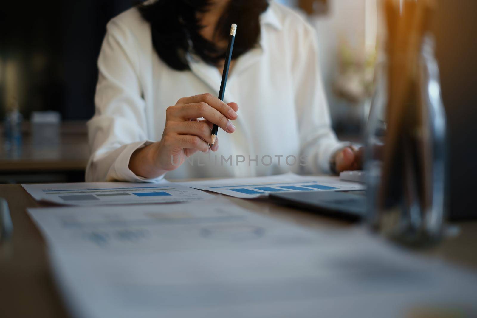 Close up Business woman hand holding pen and pointing at financial paperwork with financial paperwork.