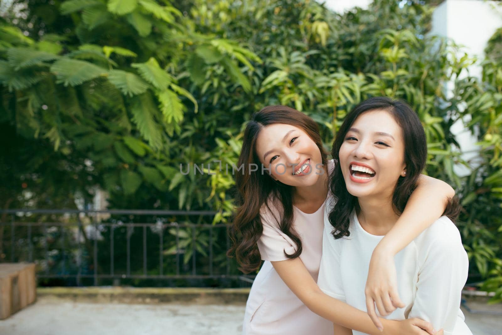 Beauties in style. Two beautiful young well-dressed women smiling at camera while standing embracing outdoors