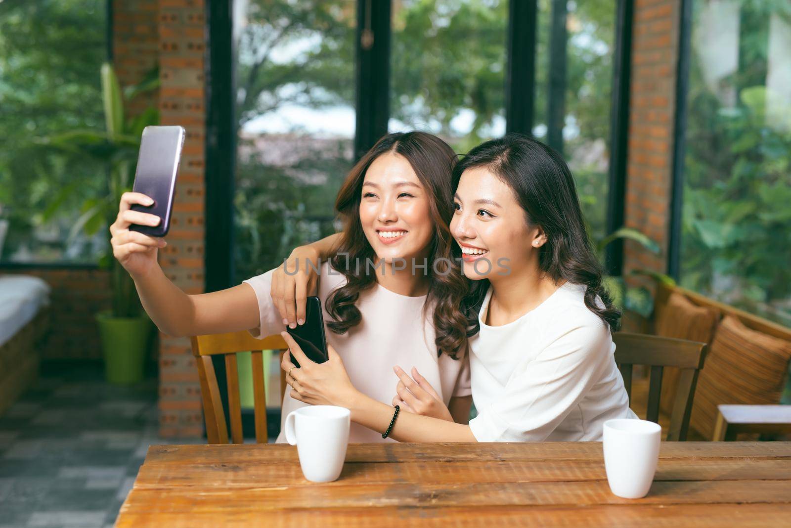 Two young and attractive females taking selfie while sitting in the cafe. by makidotvn