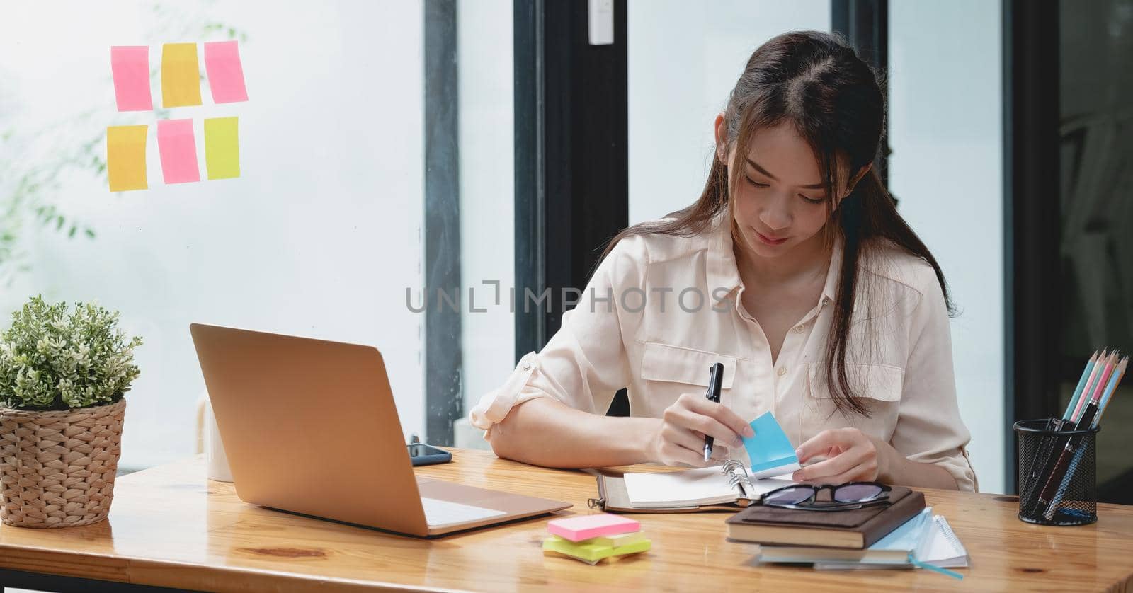 Business asian woman taking note on sticky note, Attractive girl working with laptop computer.