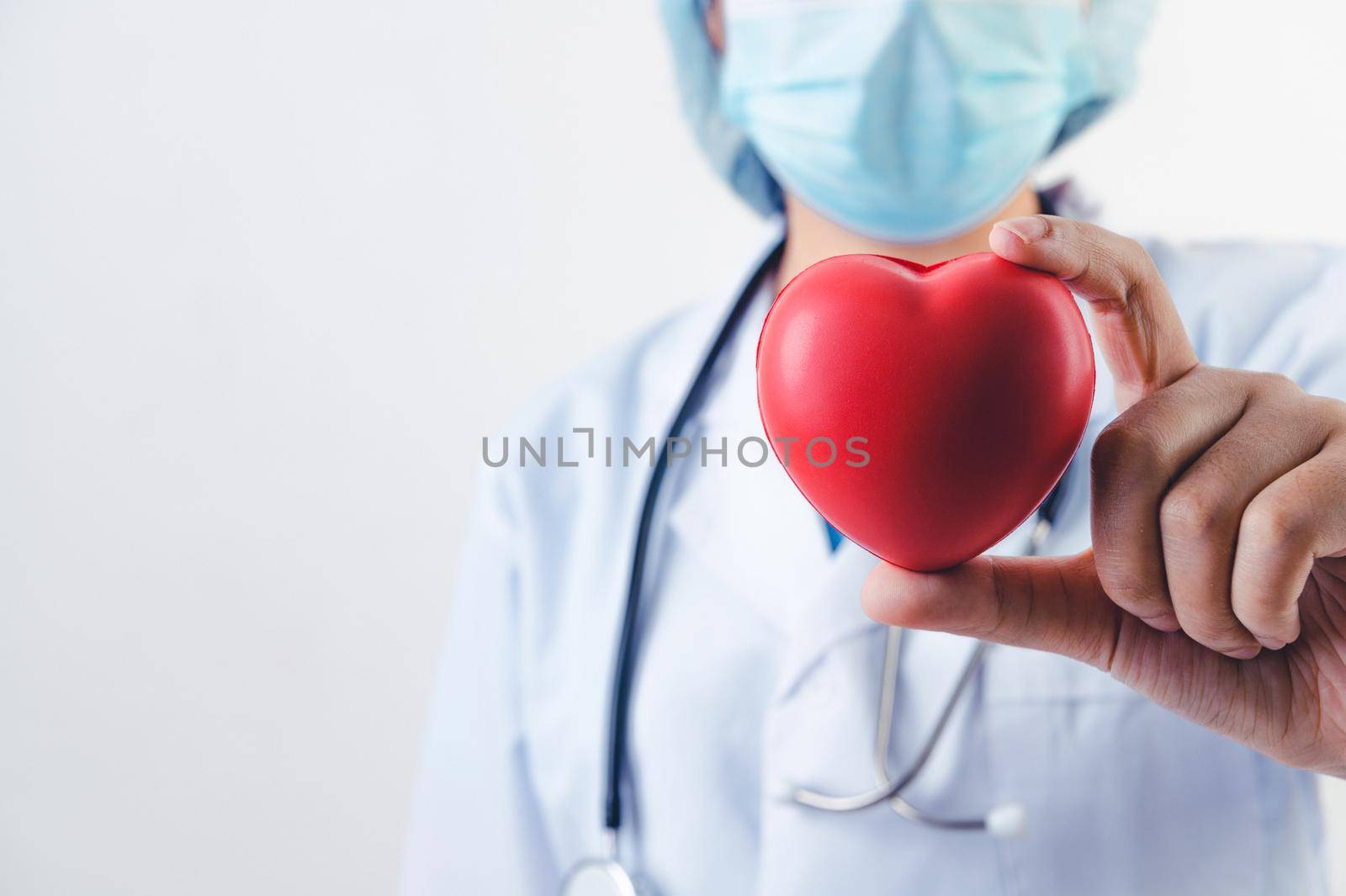 Closeup of red heart in doctor hand with stethoscope on white background. Medical people and cardio practitioner concept. Heart donation and life rescue health care theme.