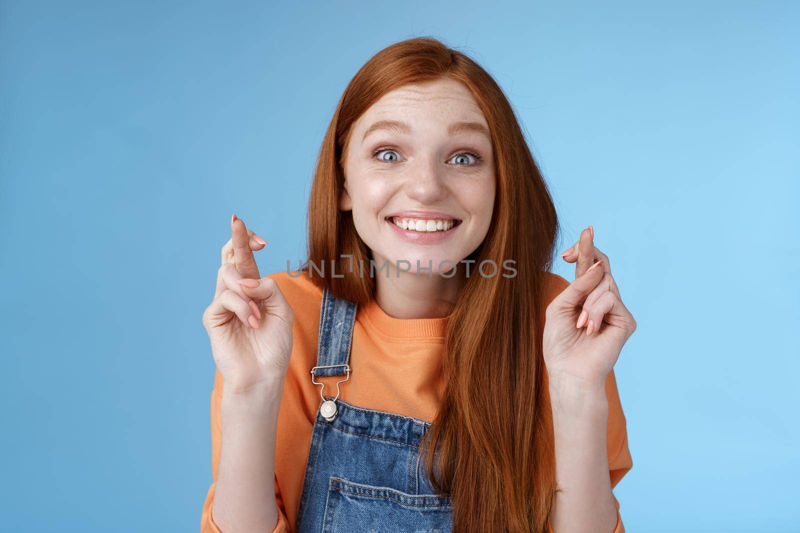 Excited emotional happy cheerful redhead girl smiling optimistic stare surprised thrilled cross fingers good luck believe dream come true make wish anticipating only good news, blue background.