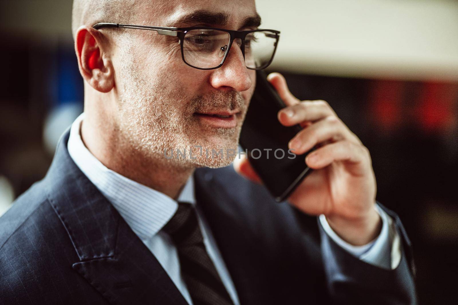 Close up. Cropped side portrait of successful mature bald man in eye glasses having business conversation on the phone with pleasant smile looking away. Business concept.