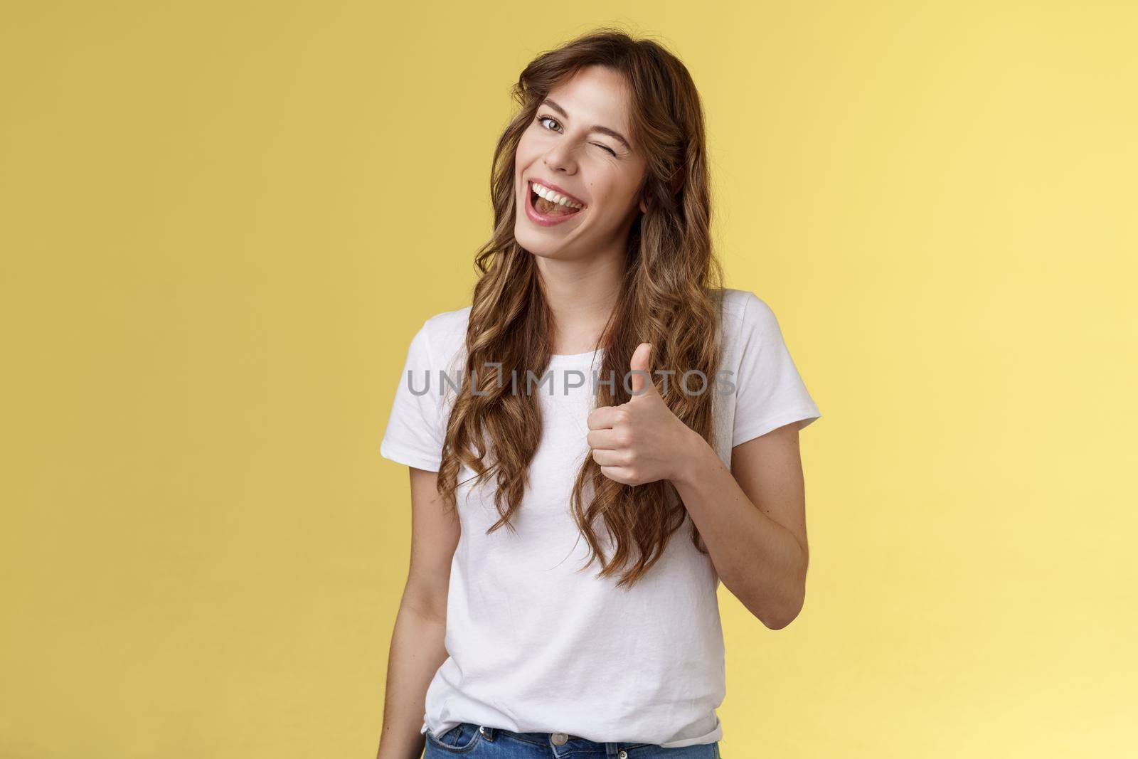 Nice well done mate. Cheerful outgoing cheeky attractive curly-haired female wink smiling nod approval show thumbs up like your choice good job accept terms stand yellow background.