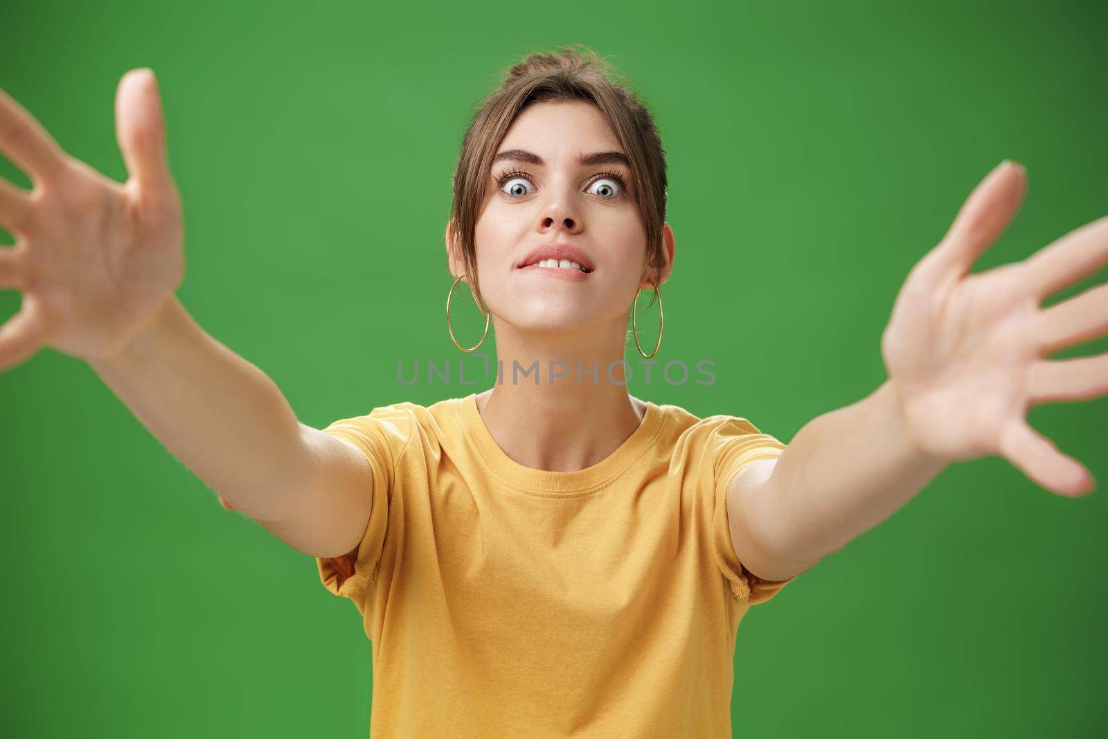 Studio shot of excited and thrilled funny womane eager to cuddle biting lower lip popping eyes at camera stretching hands towards camera with desire wanting grab thing posing over green background. Body language concept