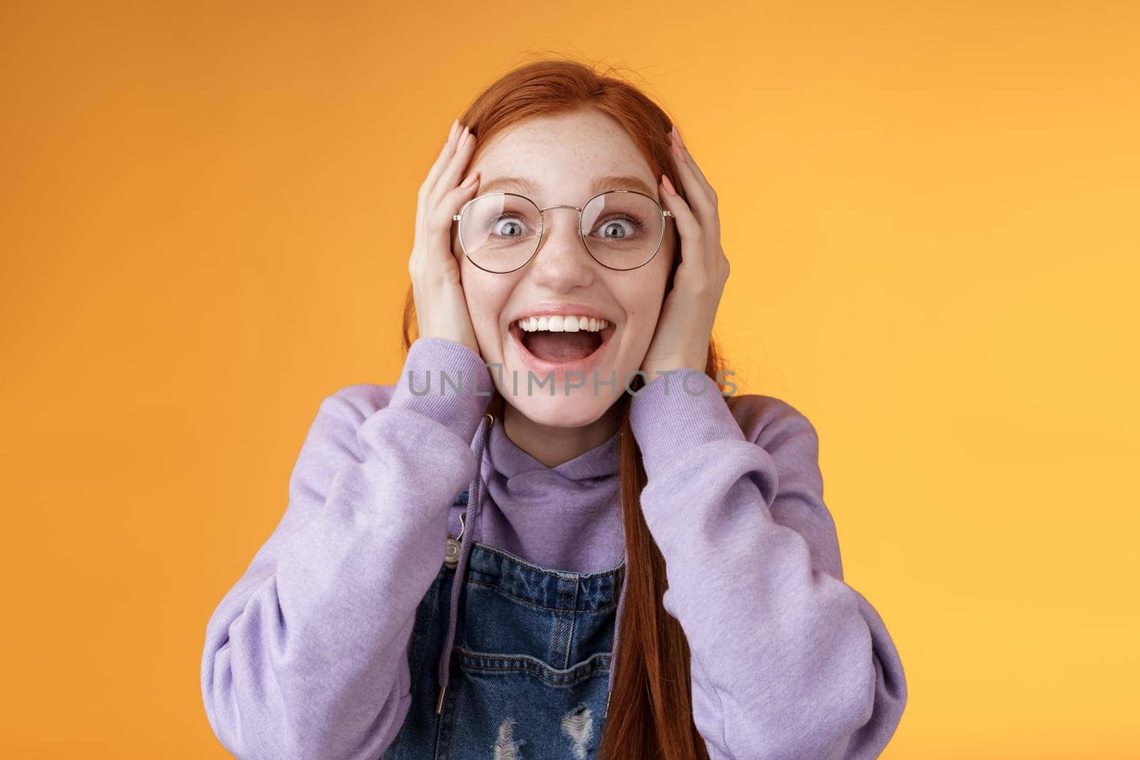 Impressed lucky cute redhead girl winner cannot believe dream come true win awesome present standing happily excited grab head smiling broadly open mouth stare surprised amazed, orange background by Benzoix