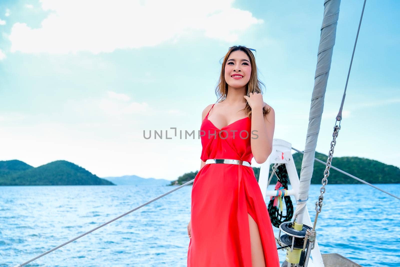 Pretty Asian woman with red dress stand on bow of yacht during boat trip during day time.