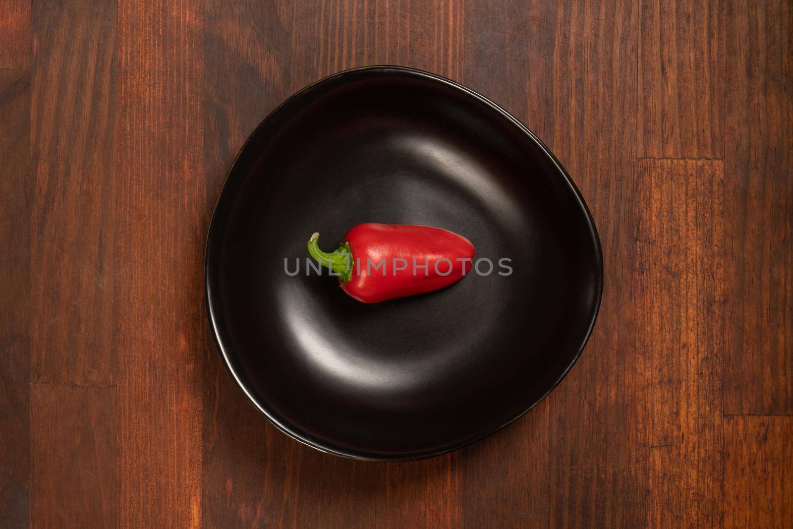 Mini red bell pepper laying in a black bawl isolated on wooden background. Top view.