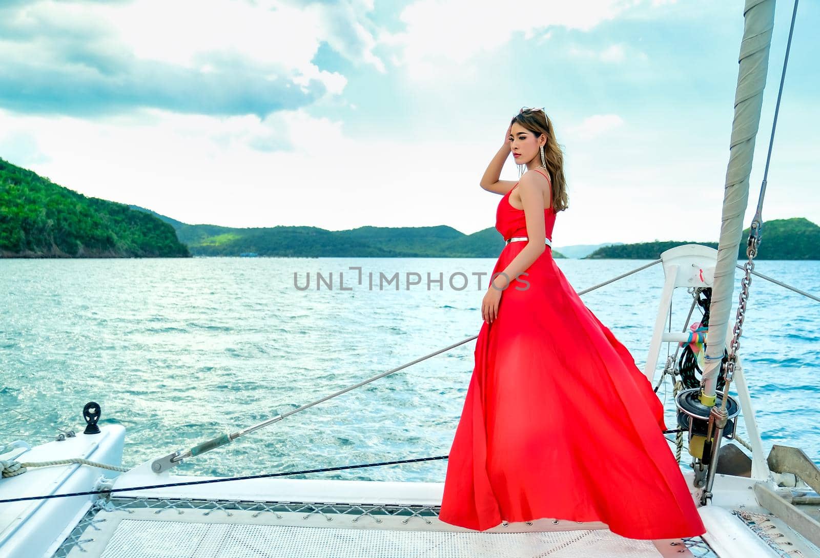 Pretty Asian woman with red dress stand on bow of yacht during boat trip during day time.