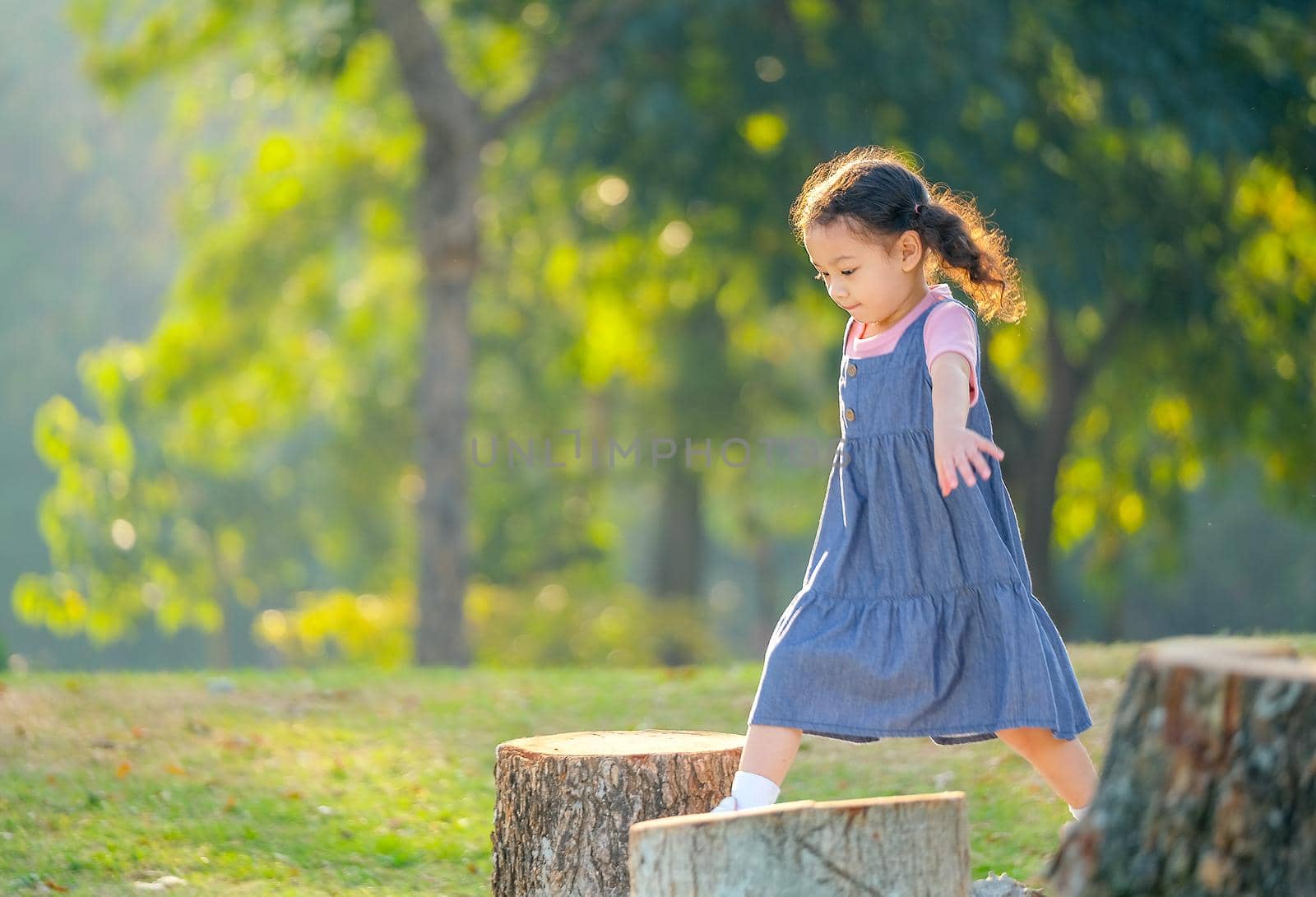 Soft blur image of young asian little girl jump and play in green garden with morning light.