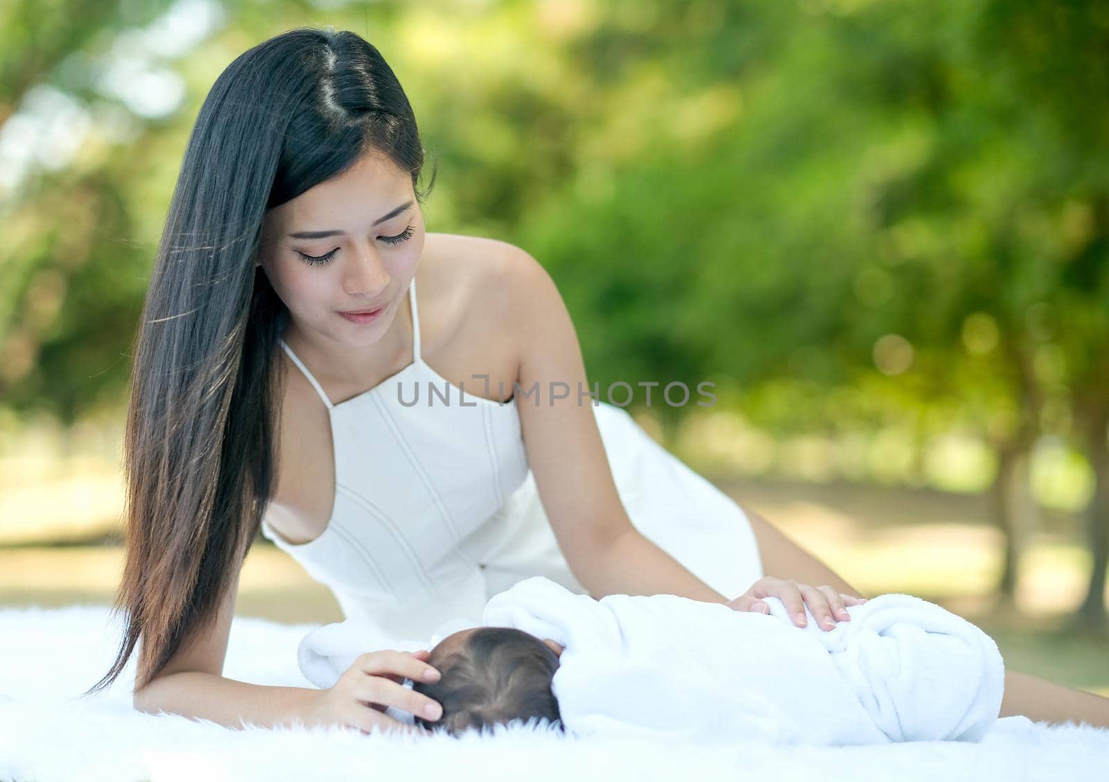 Asian beautiful mother take care her newborn baby who lie on white carpet in the garden.