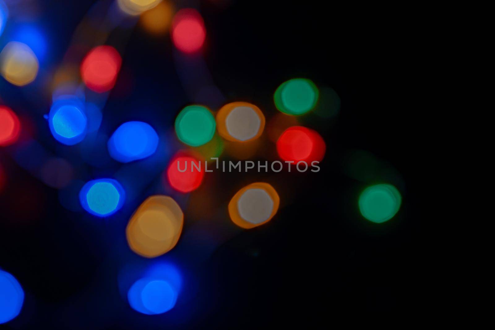 Defocused bokeh lights on black background, an abstract naturally blurred backdrop for Christmas eve or birthday party. Festive light texture. Colorful garland in blur. Overlay effect for design