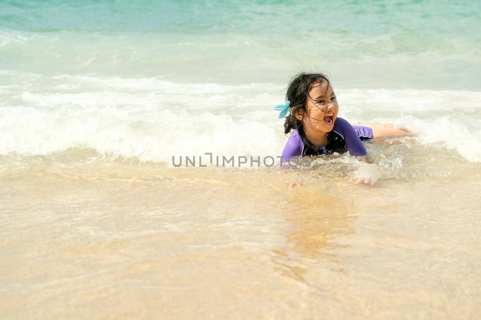 Lovely Asian little girl plays alone on beach with sea wave and she look very happy and fun.