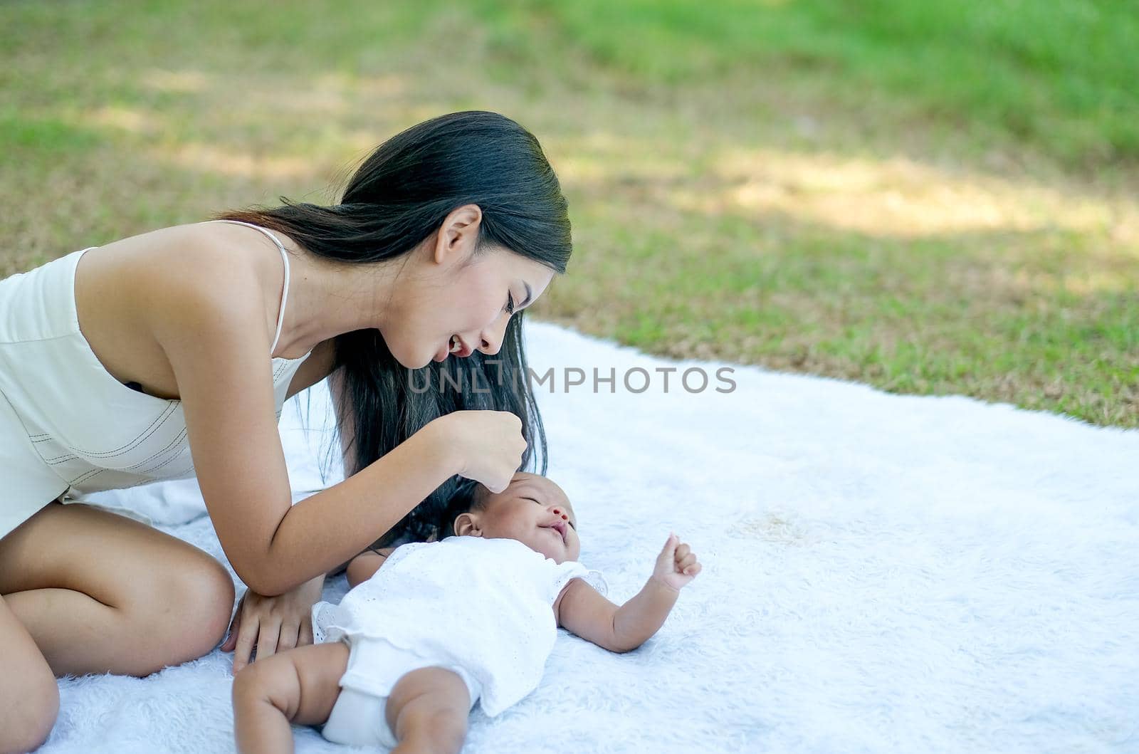 Young Asian beautiful mother play with her little baby on white carpet in the garden with morning light.