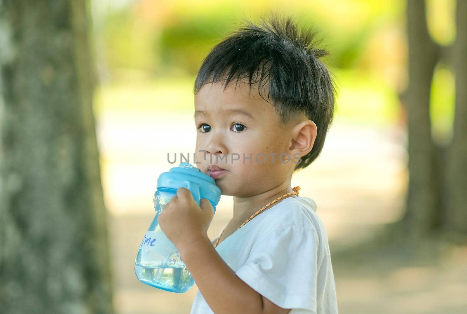 Little boy drink water from blue bottle in the green garden with day light.