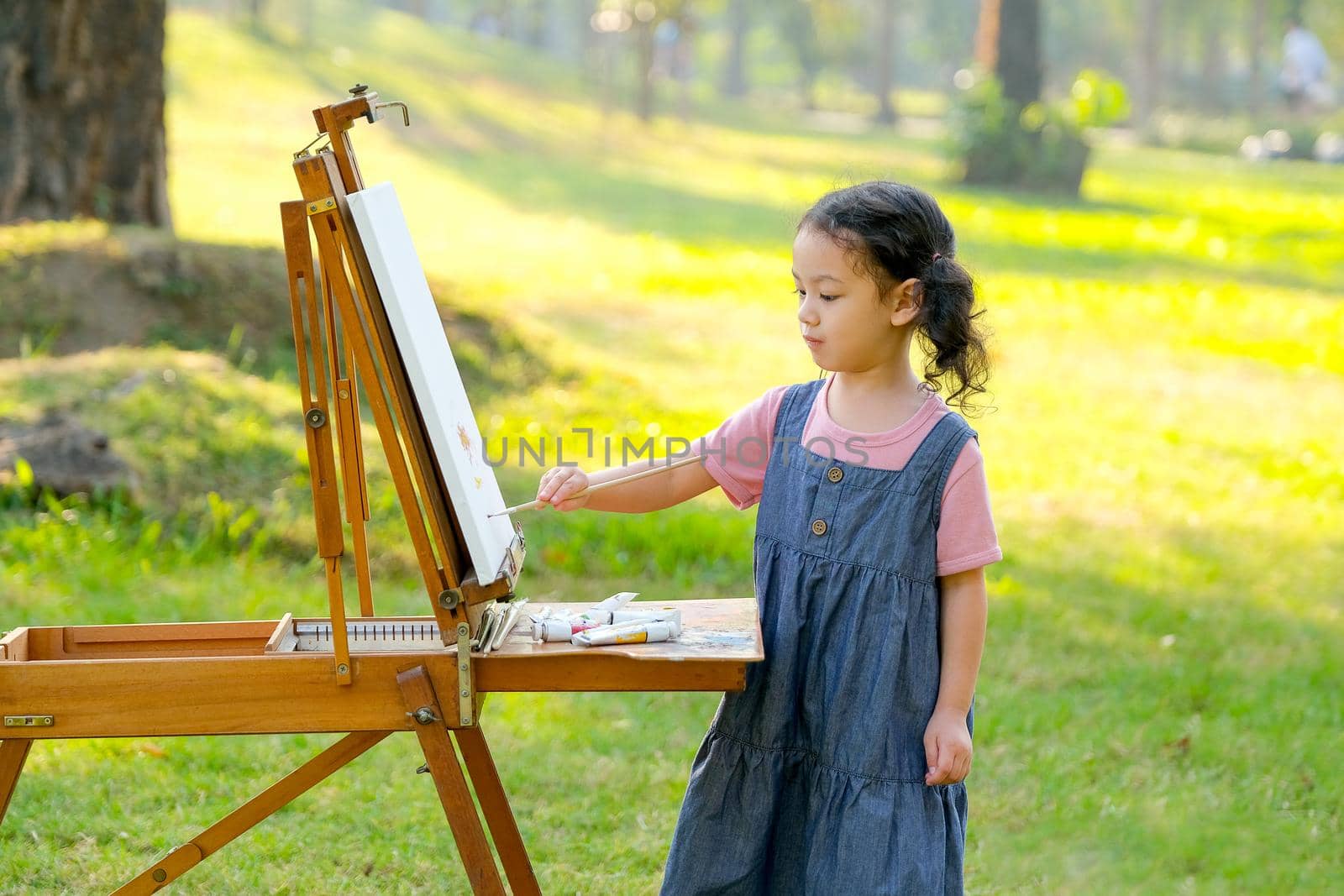 Portrait of little girl do painting in garden or park with morning light.