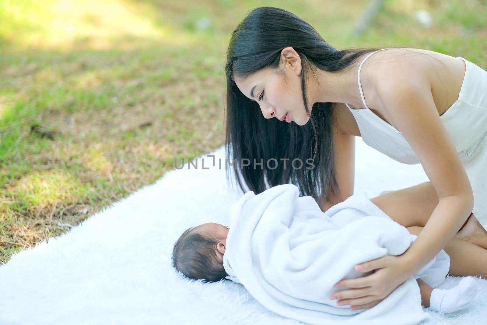 Asian beautiful mother take care her newborn baby who lie on white carpet in the garden.