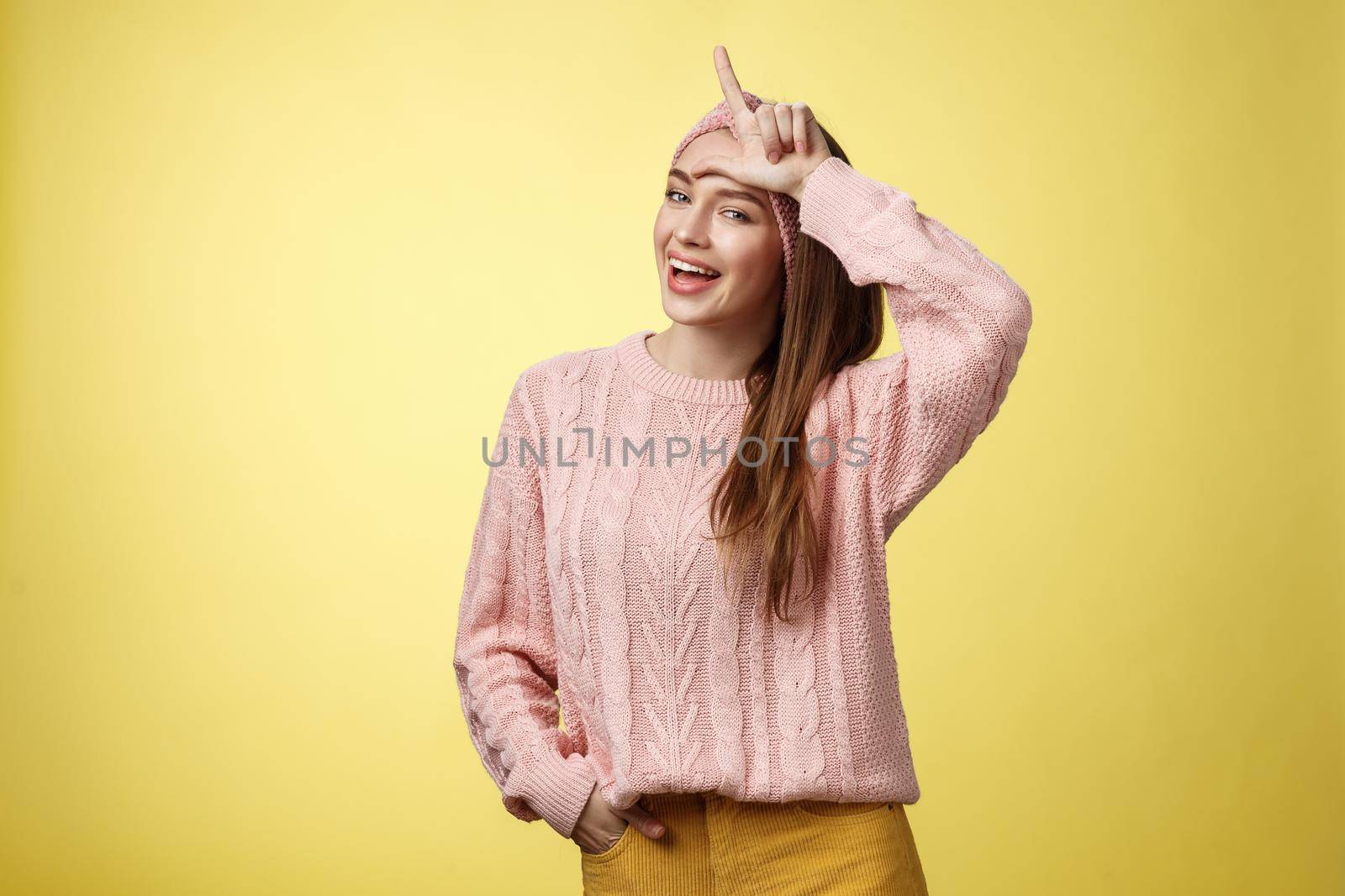 Attractive triumphing arrogant and confident cute glamourous woman in knitted sweater, headband showing l letter on forehead, loser sign and laughing over lost team, mocking having fun. Copy space