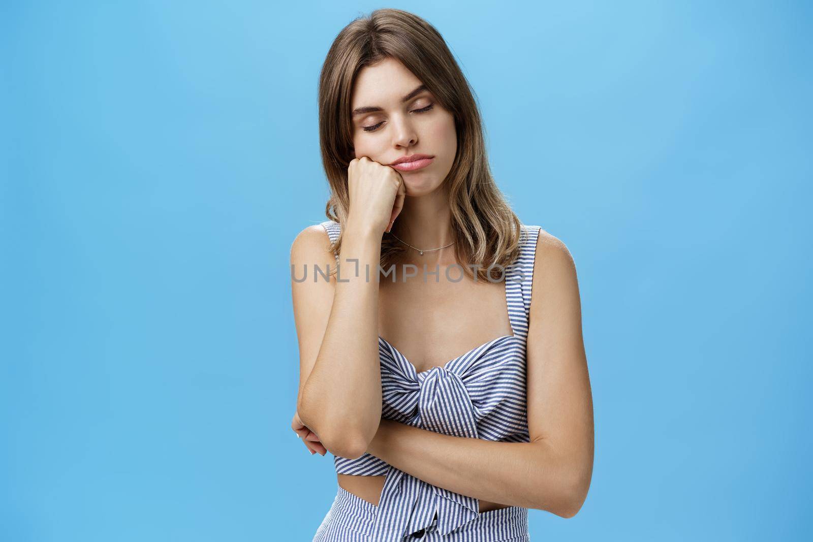 Woman standing bored and sleepy having nap while listening boring talk of boss leaning head on fist closing eyes and sleeping tired and indifferent over blue background with relaxed expression. Lifestyle.